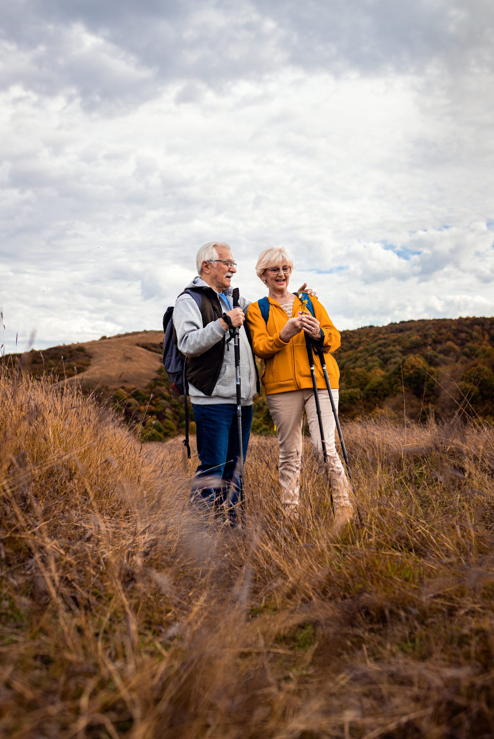 Active senior couple with backpacks hiking together in nature on autumn day.